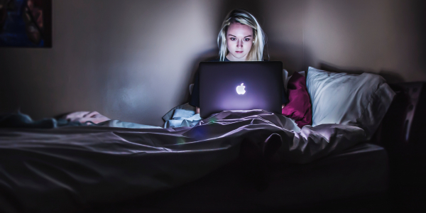 woman sitting on bed in dark room using mac laptop